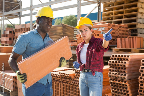 Attractive female manager pointing to african male worker where to carry bricks in a building materials warehouse