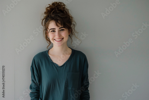Joyful Young Woman with Playful Hair Updo Smiling in Casual Clothing Against a Soft Neutral Background