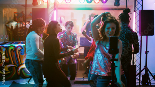 Foto Happy girl recording vlog for internet, using mobile phone at discotheque on dance floor