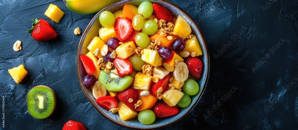 A top view of a bowl containing a vibrant fruit salad filled with pineapple, mango, grape, strawberry, papaya, melon, banana, kiwi, chestnuts, and granola, alongside a banana. A top view of a bowl containing a vibrant fruit salad filled with pineapple, mango, grape, strawberry, papaya, melon, banana, kiwi, chestnuts, and granola, alongside a banana.