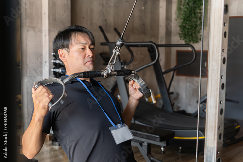 ジム・トレーニングジムで背中を鍛えるスタッフ・トレーナーのアジア人男性 