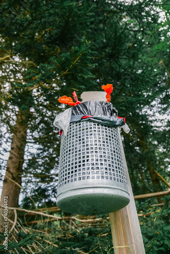 Clean forest concept. Trash in the forest. Metal trash can full of garbage in a pine spruce forest. Garbage collection in forests and natural areas. Garbage in the natural environment. Ecological photo