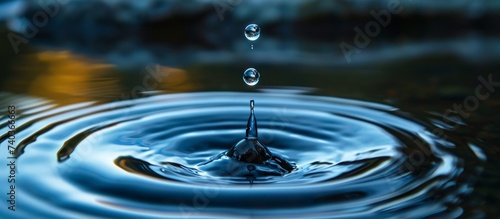 A liquid drop of water is plunging into a pool of aqua fluid, creating ripples in the electric blue circle of the solvent. Closeup view