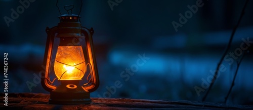 An amber lantern is emitting heat as it sits on a wooden table, providing a warm glow in the dark. The gaspowered lamp contrasts with the night sky above