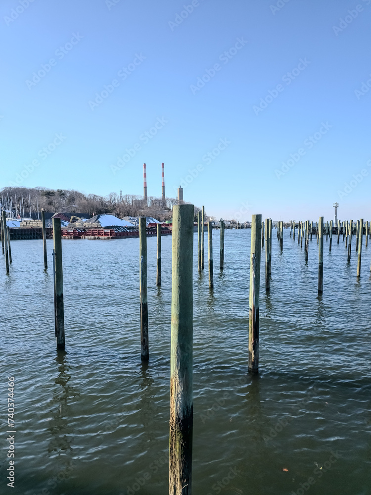 Tranquil marina scene with old wooden pier pillars standing in calm waters under a clear blue sky, evoking peace in Long Island 