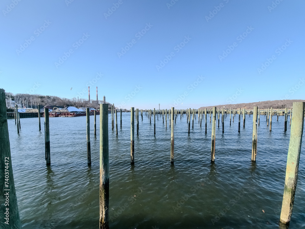 Tranquil marina scene with old wooden pier pillars standing in calm waters under a clear blue sky, evoking peace in Long Island 
