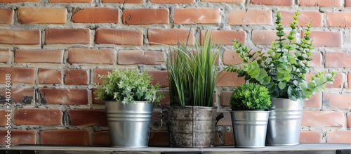 A collection of aluminum pots filled with artificial plants sitting on a wooden table, placed against a brick wall backdrop.