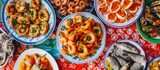 A table laden with plates of Sicilian street food, featuring calamari, octopus, fried foods, stuffed peppers, mushrooms, fish, and spicy dishes.