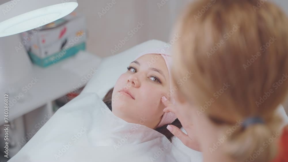 woman in modern cosmetology clinic, aesthetician examining and consulting young lady lying on couch woman in modern cosmetology clinic, aesthetician examining and consulting young lady lying on couch