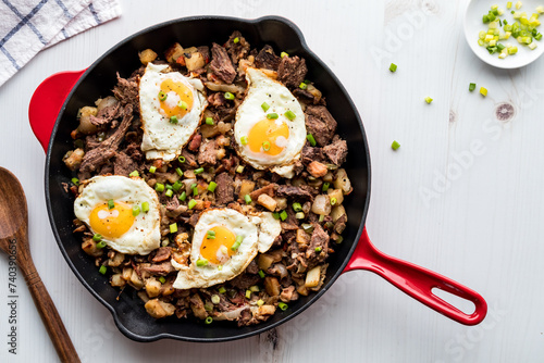 Delicious roast beef hash in a frying pan topped with fried eggs. photo