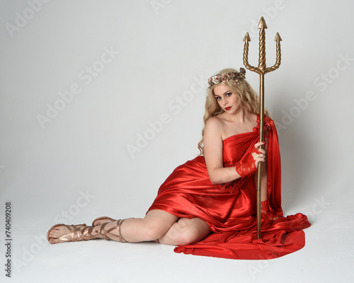 Wallpaper Mural Full length portrait of beautiful blonde model dressed as ancient mythological fantasy goddess in flowing red silk toga gown, crown. kneeling pose,  golden trident weapon, isolated studio background Torontodigital.ca