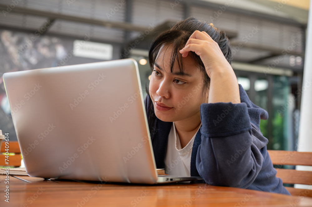 Φωτογραφία A tired Asian female is looking at her laptop screen with an unhappy face, feeling overworked