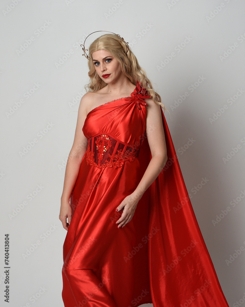close up portrait of beautiful blonde model dressed as ancient mythological fantasy goddess in flowing red silk toga gown, crown. Graceful elegant pose  holding  archery bow and arrow weapons, isolate