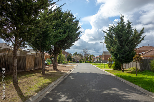 A suburban asphalt road leads to a cul-de-sac with some residential Australian homes. A street in the suburb along with family houses and trees. Melbourne VIC Australia.