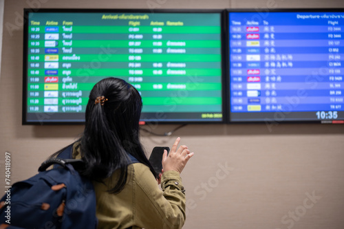 A back view shot of a female passenger checking her boarding time on a monitor screen in the airport.