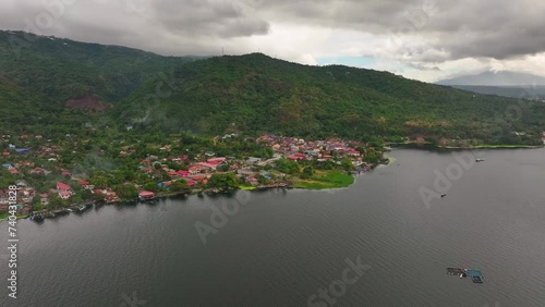 Village at Taal Lake in front of green mountains during cloudy day. Aerial approaching shot. Philippines, Asia
