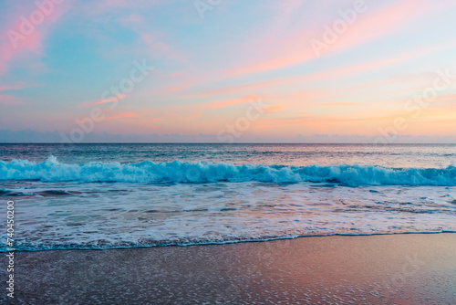 The sun sets over the tranquil beach  casting warm hues across the sky and reflecting its pink and golden glow on the waves