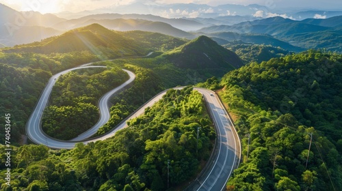 Aerial view of a winding road snaking through lush green mountains, illuminated by the warm glow of sunrise, showcasing the beauty of natural landscapes and engineering.
