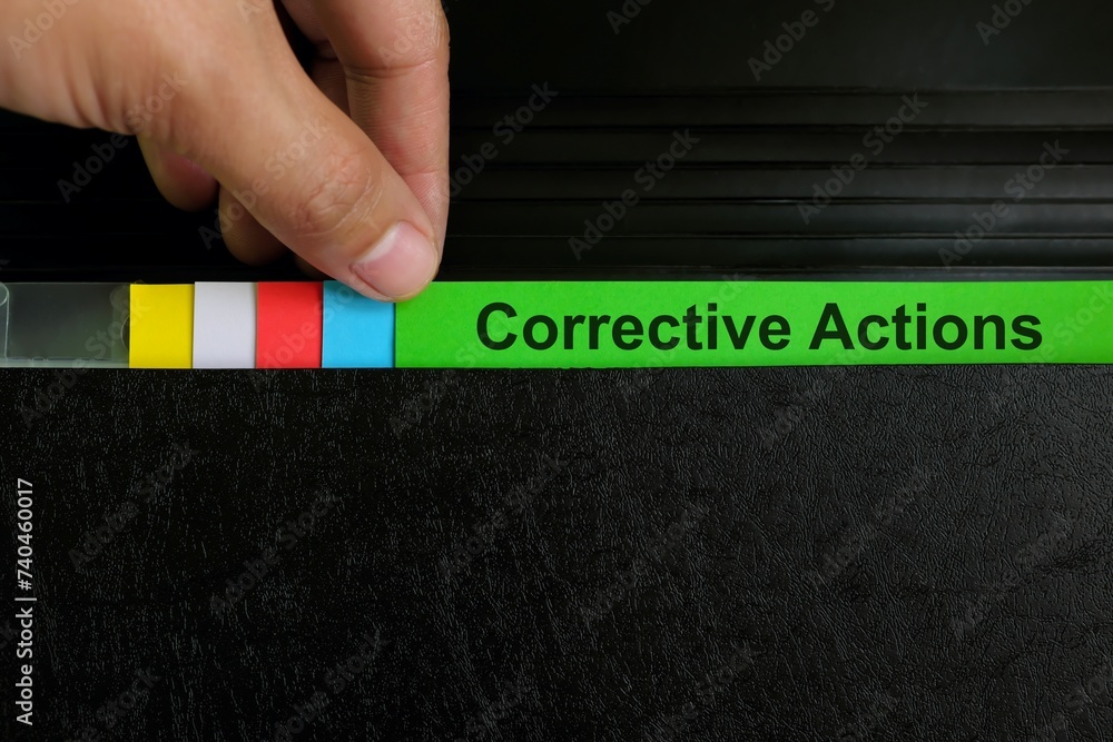 Hand picking corrective action file organizer in black background. Audit findings and root cause analysis concept.