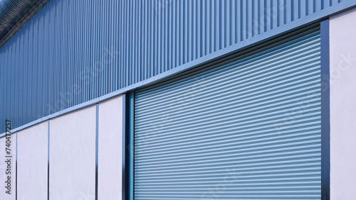 Automatic roller shutter entrance door on gray concrete and corrugated metal wall of new modern warehouse building, Perspective side view