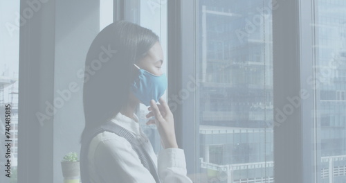 Image of financial data processing over asian businesswoman thinking with face mask in office
