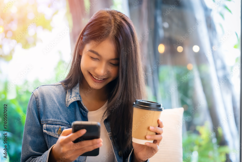 Asian woman happy and typing messages on smartphone in cafe. Smiling young woman sitting at table with hot cup of coffee and using mobile phone Asian woman happy and typing messages on smartphone in cafe. Smiling young woman sitting at table with hot cup of coffee and using mobile phone