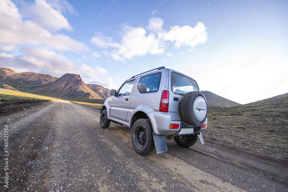 Rear view of small 4x4 on dirt road driving toward mountain highlands