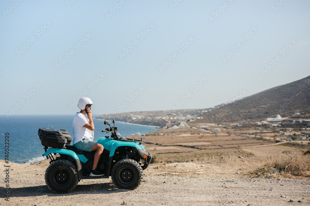 Young man adjusting helmet on four wheeler atv by coastal landscape Young man adjusting helmet on four wheeler atv by coastal landscape