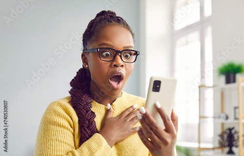 WOW. Beautiful woman looks at mobile phone with surprised open mouthed expression as she wins prize, earns money, sees unbelievable post on social media, watches shocking video, or finds special offer © Studio Romantic