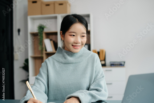 Confident Asian woman with a smile standing holding notepad and tablet at the office.