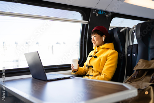 Beautiful woman traveling by train, working on laptop computer and enjoying the journey.
