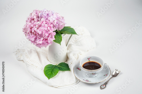 Still life with a blooming bouquet of pink hydrangea in a vase and a fine porcelain cup of coffee on a white background