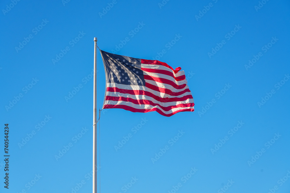 Fototapeta premium waving USA flag on pole against blue sky