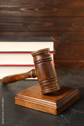 Wooden gavel and stack of books on dark textured table, closeup