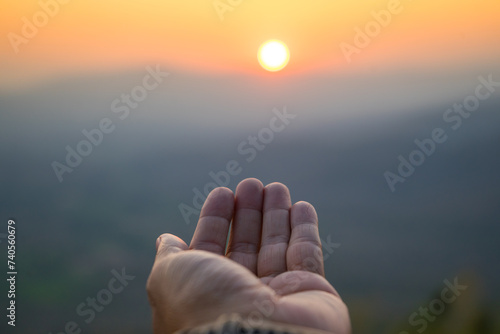 hand to reach the sun light in the morning with sea and cloud  Close the sun in your hand  Yellow light with flare light from sunrise  touch sun rays look like hope  go to success or pray for god.