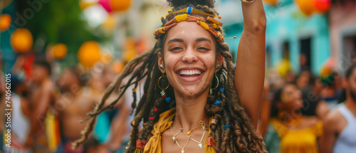 A joyful woman with dreadlocks dressed in vibrant festival clothing is dancing on the street with a blurred crowd in the background.