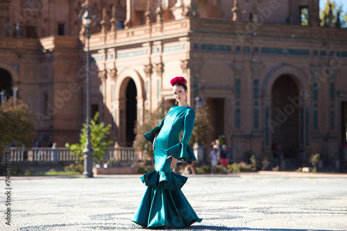 Young and beautiful woman with typical green dress with ruffles and dancing flamenco in plaza de espana in seville, andalusia, walks with art and passion. 16 november, international flamenco day. © @skuder_photographer