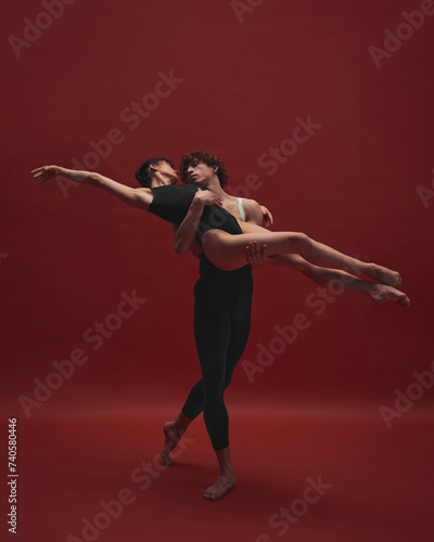 Beautiful, elegant young woman and handsome man, ballet dancer dancing against red background. Black and red. Concept of classic art, aesthetics, emotions, ballet dance, talent