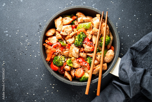 Chicken stir fry with vegetables and sesame at black background. Traditional asian cuisine.