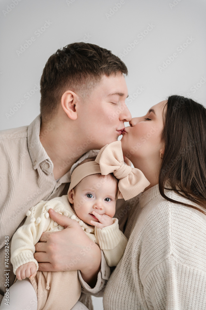 Man kisses woman. Father, mother hugging daughter. Happy family hugs cute baby on a holiday closeup. Dad, mom holds in hands 6 month old little kid. Daddy, mommy embracing girl isolated on white wall. Man kisses woman. Father, mother hugging daughter. Happy family hugs cute baby on a holiday closeup. Dad, mom holds in hands 6 month old little kid. Daddy, mommy embracing girl isolated on white wall.