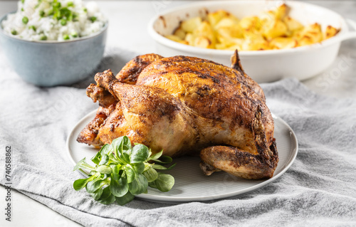 A whole roasted chicken on the table together with jasmine rice and baked potatoes.