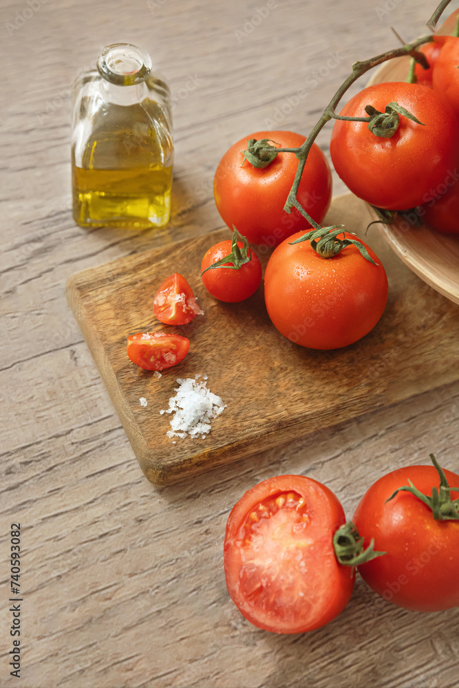 Cherry tomatoes and large tomatoes, some cut, some whole some still attached to a vine on a wooden cutting board with salt and a glass bottel of olive oil. Cherry tomatoes and large tomatoes, some cut, some whole some still attached to a vine on a wooden cutting board with salt and a glass bottel of olive oil.