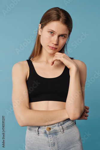 Vertical medium studio portrait of young Caucasian woman with no makeup wearing crop top and jeans looking at camera