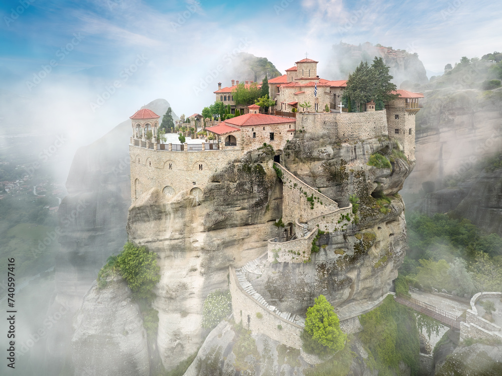 Meteora Holy Varlaam Monastery on a cliff rising out of the mist against blue sky. Red roofs, nobody, mystical athmosphere. A UNESCO heritage site. Meteora mountains, Greece. Meteora Holy Varlaam Monastery on a cliff rising out of the mist against blue sky. Red roofs, nobody, mystical athmosphere. A UNESCO heritage site. Meteora mountains, Greece.