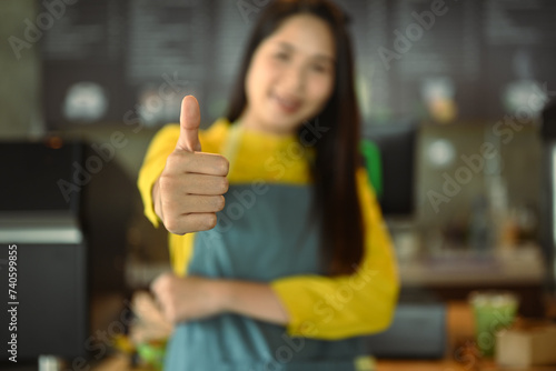 Smiling small business owner in apron showing thumbs up standing at her coffee shop