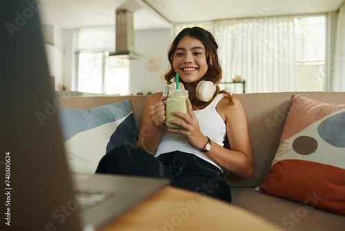 Smiling teenage girl drinking smoothie and watching show on laptop