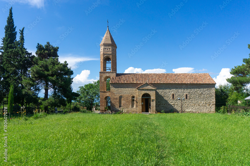 Saint Giorgi church on a green grass lawn against the background of a blue sky with clouds.