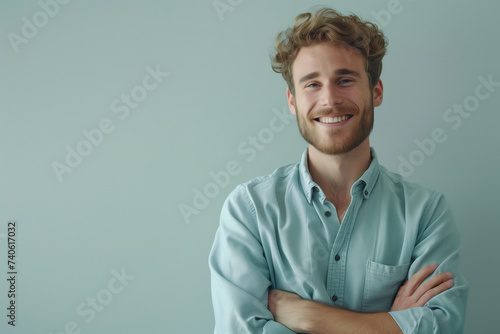Charming Young Man with a Joyful Smile Wearing a Light Blue Shirt Posing with Arms Crossed on a Gradient Background