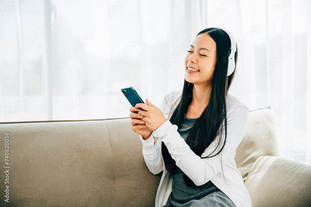 Woman with smartphone and headphones relaxes on sofa listens to music. Engaged in leisure enjoyment and technology at home. Entertainment concept. Woman with smartphone and headphones relaxes on sofa listens to music. Engaged in leisure enjoyment and technology at home. Entertainment concept.