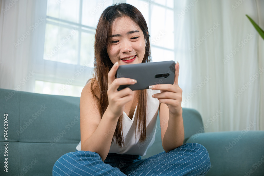 Smiling female sitting comfortably on sofa using mobile smart phone for shopping online at living room at home, Happy young woman relaxed and messaging smartphone, checking social media networks Smiling female sitting comfortably on sofa using mobile smart phone for shopping online at living room at home, Happy young woman relaxed and messaging smartphone, checking social media networks